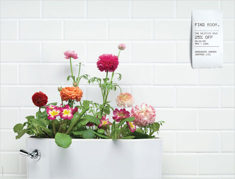 Bright pink and orange flowers planted in a toilet tank with receipt on the wall